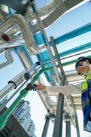 Industrial engineer adjusting pipeline valve with radio communication on construction site. Engineer on urban construction site using radio to coordinate with team on a sunny industrial rooftop. photo