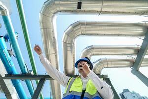 Industrial engineer adjusting pipeline valve with radio communication on construction site. Engineer on urban construction site using radio to coordinate with team on a sunny industrial rooftop. photo