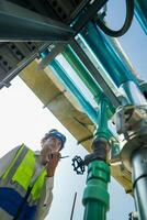 Industrial engineer adjusting pipeline valve with radio communication on construction site. Construction worker using walkie-talkie to coordinate machinery adjustments on a sunny day. photo