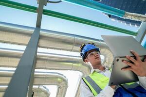 Industrial engineer adjusting pipeline valve with radio communication on construction site. Engineer on urban construction site using radio to coordinate with team on a sunny industrial rooftop. photo
