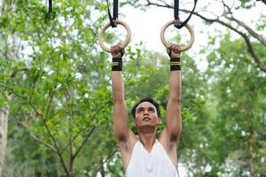 Asian man practicing gymnastics doing gymnastics bar and hoop exercises and stretching and resting for sports. photo