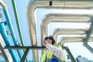 Industrial engineer adjusting pipeline valve with radio communication on construction site. Engineer on urban construction site using radio to coordinate with team on a sunny industrial rooftop. photo