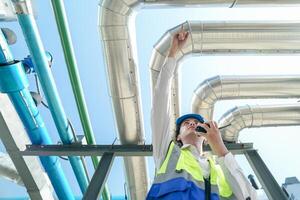 Industrial engineer adjusting pipeline valve with radio communication on construction site. Engineer on urban construction site using radio to coordinate with team on a sunny industrial rooftop. photo