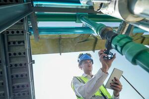 Male engineer monitoring machinery on a rooftop with city skyline in the background, wearing safety gear photo