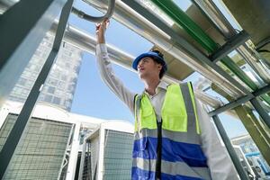 Industrial engineer adjusting pipeline valve with radio communication on construction site. Engineer on urban construction site using radio to coordinate with team on a sunny industrial rooftop. photo