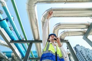 Industrial engineer adjusting pipeline valve with radio communication on construction site. Engineer on urban construction site using radio to coordinate with team on a sunny industrial rooftop. photo