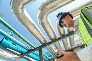 Industrial engineer adjusting pipeline valve with radio communication on construction site. Engineer on urban construction site using radio to coordinate with team on a sunny industrial rooftop. photo