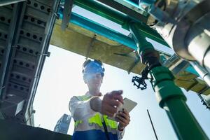 Industrial engineer adjusting pipeline valve with radio communication on construction site. Construction worker using walkie-talkie to coordinate machinery adjustments on a sunny day. photo