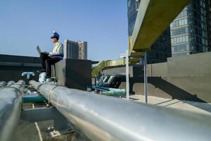 ingeniero en edificio techo con computadora portátil, supervisando urbano construcción, azul cielo, y rascacielos foto