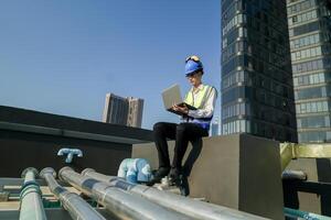 ingeniero en edificio techo con computadora portátil, supervisando urbano construcción, azul cielo, y rascacielos foto