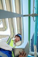 Industrial engineer adjusting pipeline valve with radio communication on construction site. Engineer on urban construction site using radio to coordinate with team on a sunny industrial rooftop. photo