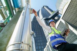 Industrial engineer adjusting pipeline valve with radio communication on construction site. Engineer on urban construction site using radio to coordinate with team on a sunny industrial rooftop. photo