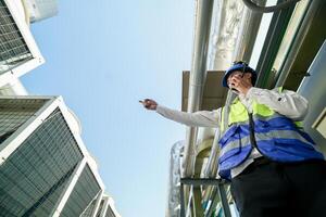Industrial engineer adjusting pipeline valve with radio communication on construction site. Engineer on urban construction site using radio to coordinate with team on a sunny industrial rooftop. photo