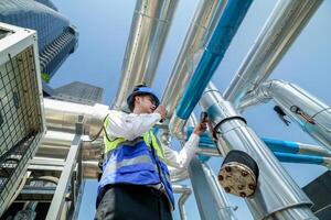Industrial engineer adjusting pipeline valve with radio communication on construction site. Engineer on urban construction site using radio to coordinate with team on a sunny industrial rooftop. photo