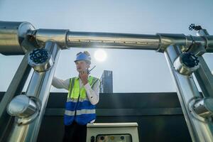 Engineer in safety gear conducts inspection on large industrial water tanks on a building rooftop. Professional engineer meticulously checks connectivity and status of piping on an urban rooftop. photo