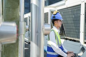 Industrial engineer adjusting pipeline valve with radio communication on construction site. Engineer on urban construction site using radio to coordinate with team on a sunny industrial rooftop. photo