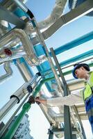 Industrial engineer adjusting pipeline valve with radio communication on construction site. Engineer on urban construction site using radio to coordinate with team on a sunny industrial rooftop. photo