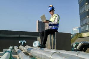 ingeniero en edificio techo con computadora portátil, supervisando urbano construcción, azul cielo, y rascacielos foto