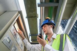 Industrial engineer adjusting pipeline valve with radio communication on construction site. Engineer on urban construction site using radio to coordinate with team on a sunny industrial rooftop. photo
