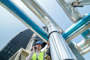 Industrial engineer adjusting pipeline valve with radio communication on construction site. Engineer on urban construction site using radio to coordinate with team on a sunny industrial rooftop. photo