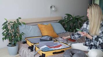 A woman carefully packs things into a yellow suitcase while checking the list on her smartphone. video