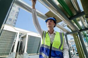 Industrial engineer adjusting pipeline valve with radio communication on construction site. Engineer on urban construction site using radio to coordinate with team on a sunny industrial rooftop. photo