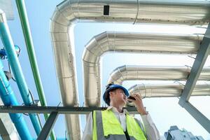 Industrial engineer adjusting pipeline valve with radio communication on construction site. Engineer on urban construction site using radio to coordinate with team on a sunny industrial rooftop. photo