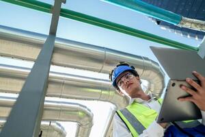 Industrial engineer adjusting pipeline valve with radio communication on construction site. Engineer on urban construction site using radio to coordinate with team on a sunny industrial rooftop. photo