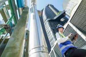Industrial engineer adjusting pipeline valve with radio communication on construction site. Engineer on urban construction site using radio to coordinate with team on a sunny industrial rooftop. photo