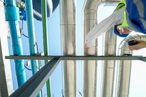 Industrial engineer adjusting pipeline valve with radio communication on construction site. Engineer on urban construction site using radio to coordinate with team on a sunny industrial rooftop. photo