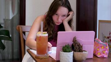 Online learning girl in a cafe working on a pink tablet writing down mathematical equations with a pen drinking a cocktail in a tropical country relaxing while studying study online video