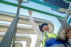 Industrial engineer adjusting pipeline valve with radio communication on construction site. Engineer on urban construction site using radio to coordinate with team on a sunny industrial rooftop. photo