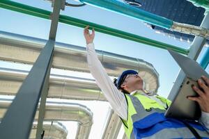 Industrial engineer adjusting pipeline valve with radio communication on construction site. Engineer on urban construction site using radio to coordinate with team on a sunny industrial rooftop. photo