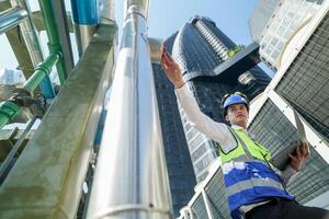 Industrial engineer adjusting pipeline valve with radio communication on construction site. Engineer on urban construction site using radio to coordinate with team on a sunny industrial rooftop. photo
