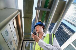Industrial engineer adjusting pipeline valve with radio communication on construction site. Engineer on urban construction site using radio to coordinate with team on a sunny industrial rooftop. photo