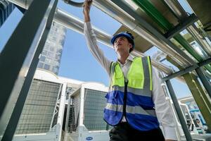 Industrial engineer adjusting pipeline valve with radio communication on construction site. Engineer on urban construction site using radio to coordinate with team on a sunny industrial rooftop. photo