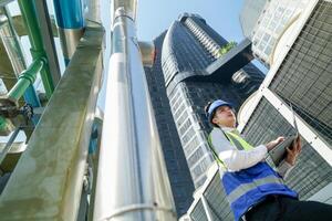 Industrial engineer adjusting pipeline valve with radio communication on construction site. Engineer on urban construction site using radio to coordinate with team on a sunny industrial rooftop. photo