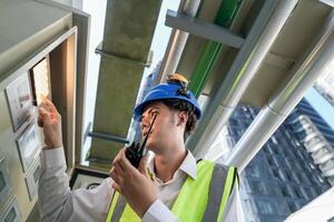Industrial engineer adjusting pipeline valve with radio communication on construction site. Engineer on urban construction site using radio to coordinate with team on a sunny industrial rooftop. photo