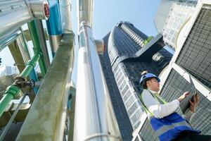 Industrial engineer adjusting pipeline valve with radio communication on construction site. Engineer on urban construction site using radio to coordinate with team on a sunny industrial rooftop. photo