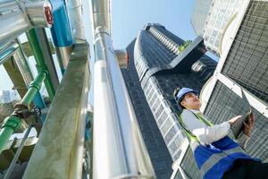 Industrial engineer adjusting pipeline valve with radio communication on construction site. Engineer on urban construction site using radio to coordinate with team on a sunny industrial rooftop. photo