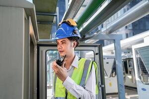 Industrial engineer adjusting pipeline valve with radio communication on construction site. Engineer on urban construction site using radio to coordinate with team on a sunny industrial rooftop. photo