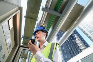Industrial engineer adjusting pipeline valve with radio communication on construction site. Engineer on urban construction site using radio to coordinate with team on a sunny industrial rooftop. photo