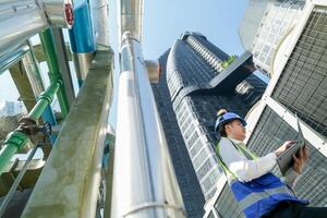 Industrial engineer adjusting pipeline valve with radio communication on construction site. Engineer on urban construction site using radio to coordinate with team on a sunny industrial rooftop. photo