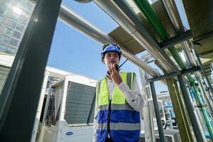Industrial engineer adjusting pipeline valve with radio communication on construction site. Engineer on urban construction site using radio to coordinate with team on a sunny industrial rooftop. photo