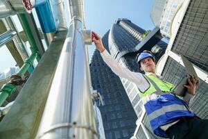 Industrial engineer adjusting pipeline valve with radio communication on construction site. Engineer on urban construction site using radio to coordinate with team on a sunny industrial rooftop. photo
