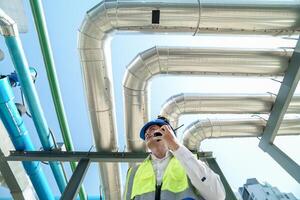 Industrial engineer adjusting pipeline valve with radio communication on construction site. Engineer on urban construction site using radio to coordinate with team on a sunny industrial rooftop. photo