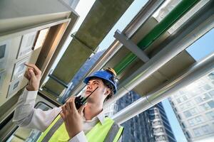Industrial engineer adjusting pipeline valve with radio communication on construction site. Engineer on urban construction site using radio to coordinate with team on a sunny industrial rooftop. photo