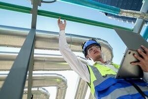 Industrial engineer adjusting pipeline valve with radio communication on construction site. Engineer on urban construction site using radio to coordinate with team on a sunny industrial rooftop. photo
