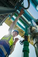 Industrial engineer adjusting pipeline valve with radio communication on construction site. Construction worker using walkie-talkie to coordinate machinery adjustments on a sunny day. photo