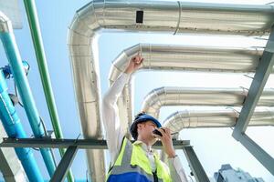 Industrial engineer adjusting pipeline valve with radio communication on construction site. Engineer on urban construction site using radio to coordinate with team on a sunny industrial rooftop. photo